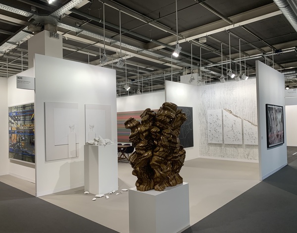 big event hall with grey carpet flooring and white art exhibition stands, brown sculpture in foreground
