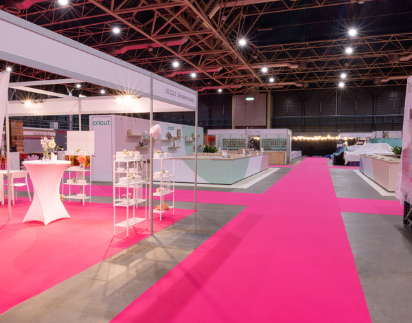 white standing booths at exhibition with bright pink event carpet pathways inside of a big event venue