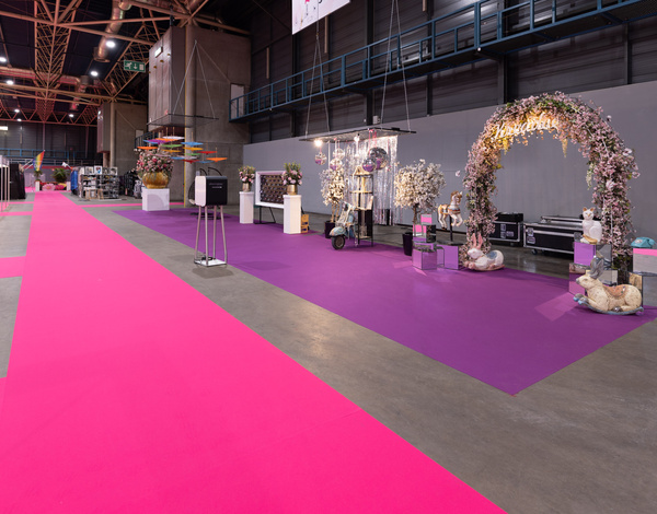 Creative exhibitions inside big event hall, an arch with flowers on purple event carpet next to a pink carpet path