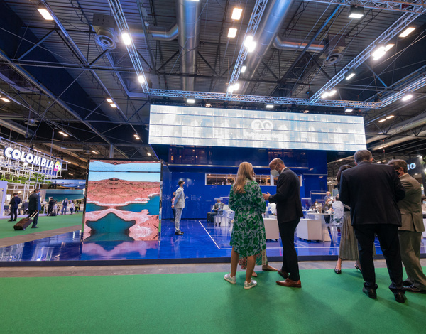 inside of a big event hall with screens and people standing at the foreground, blue and green flooring