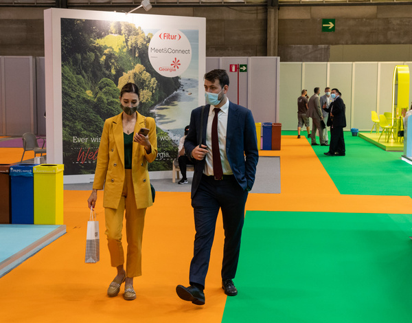 Two people walking on orange and green event carpet pathway between exhibition stands 