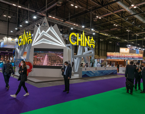 People standing near exhibition stand with lights saying China, big event building with green and purple carpet